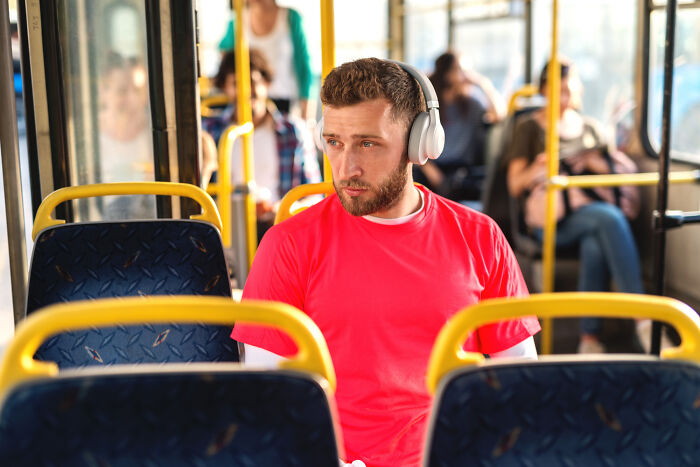 A man wearing headphones on a bus, keeping a secret, looking away with a pensive expression.