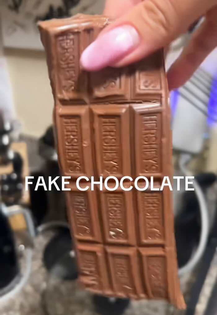 A hand holding a Hershey's chocolate bar, which is labeled as fake chocolate, highlighting fake foods Americans eat. A hand holding a Hershey's chocolate bar, which is labeled as fake chocolate, highlighting fake foods Americans eat.