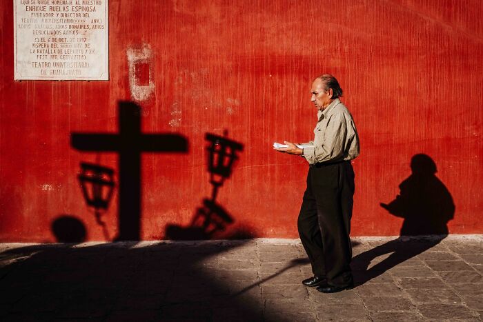 A man walks past a red wall with cross shadows, a dramatic street photography award winning image.