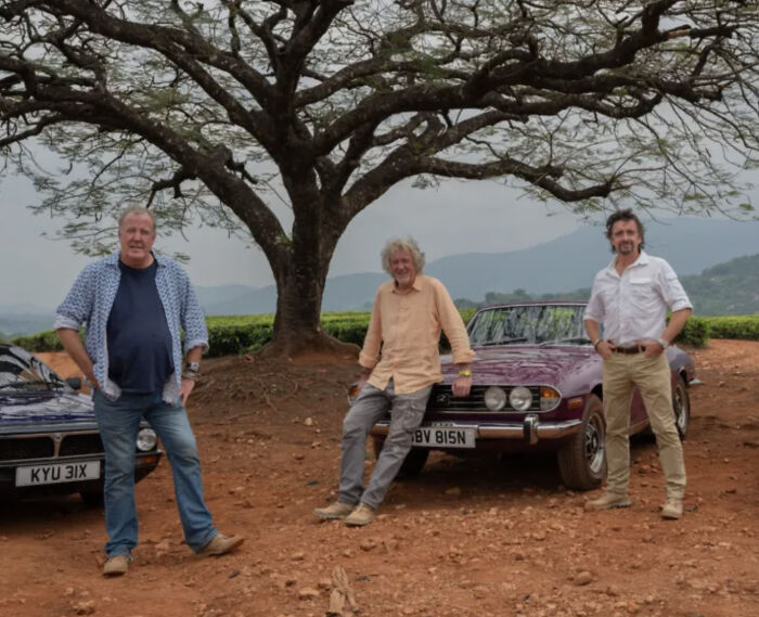 Three men stand with classic cars under a large tree, showcasing dry British humor.