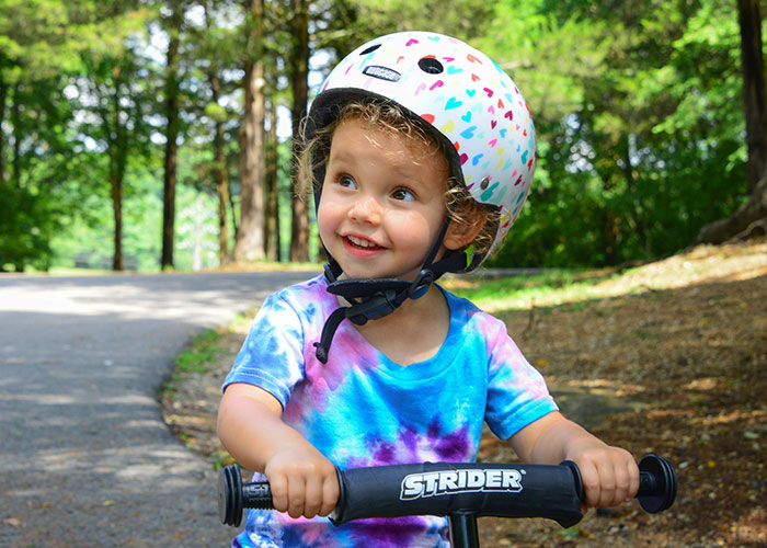 A happy young child wearing a helmet on a balance bike. A doctor shares five things parents should not allow children to do.