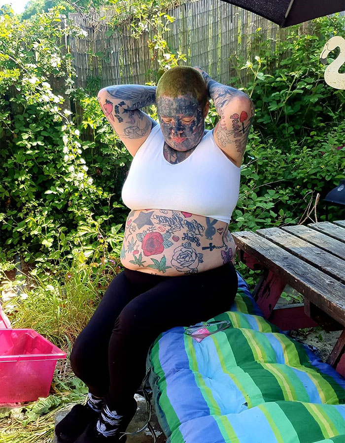 A mom with 800 tattoos sits outdoors, revealing her face and body tattoos without the extreme look. A mom with 800 tattoos sits outdoors, revealing her face and body tattoos without the extreme look.