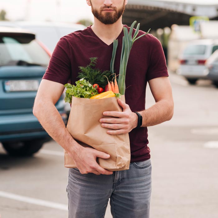 A man with a beard holds a brown paper bag full of fresh groceries, reflecting on dumb work rules.