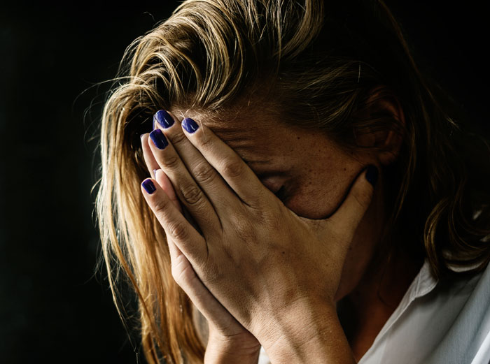 A woman with hands over her face, appearing upset or embarrassed by things that happened at weddings.