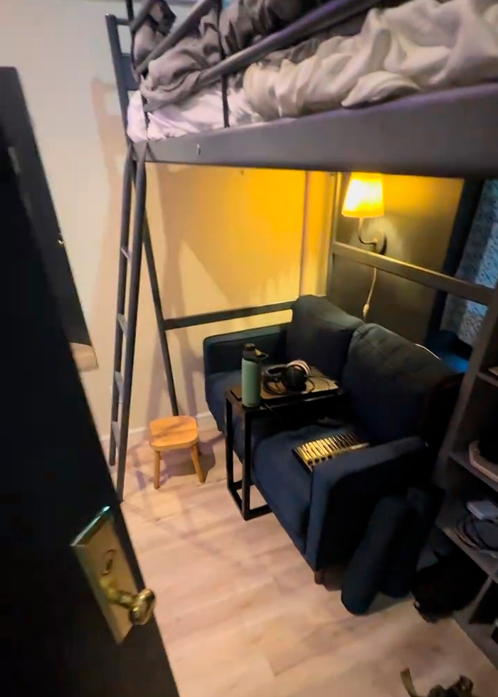 An interior view of the 90-square-foot NYC apartment, showing a bed, a small couch, and a ladder leading to the loft bed, emphasizing the harsh reality of the urban prison cell. An interior view of the 90-square-foot NYC apartment, showing a bed, a small couch, and a ladder leading to the loft bed, emphasizing the harsh reality of the urban prison cell.