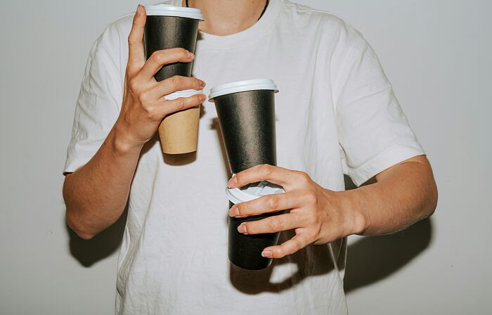 A person holding two large coffee cups, suggesting a routine of coffee consumption and habits.
