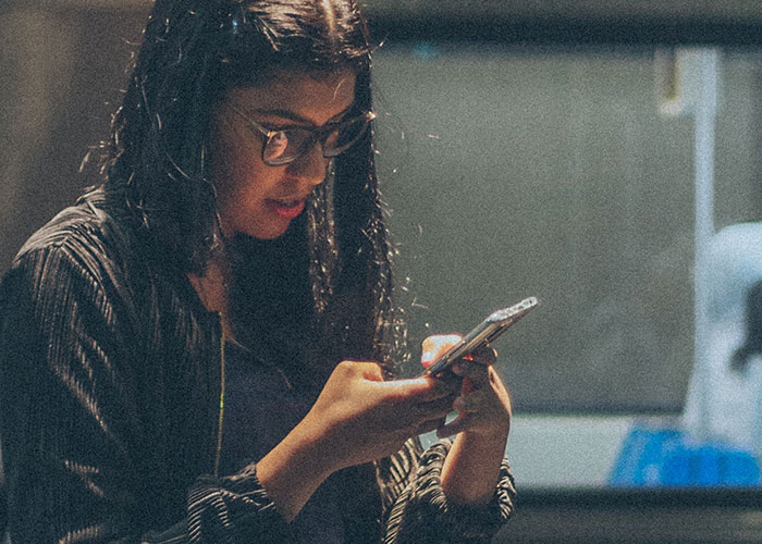 A woman wearing glasses engrossed in her phone, likely reflecting on worst first dates with women.