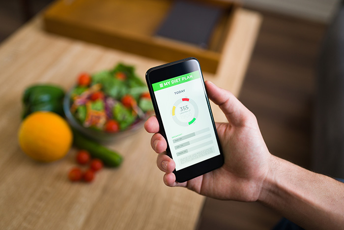 A hand holding a smartphone showing a diet plan app with healthy food in the background.