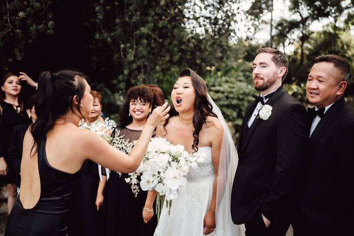 Funny wedding photo of a bride playfully eating a berry from a guest at her wedding.
