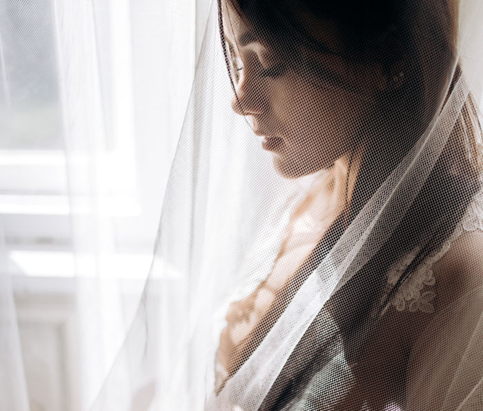 A pensive bride is partially obscured by a delicate white veil, reflecting on her wedding and fiancée. A pensive bride is partially obscured by a delicate white veil, reflecting on her wedding and fiancée.
