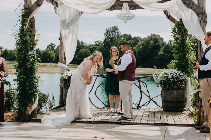 Funny wedding photo of a bride laughing during an outdoor ceremony by a lake.