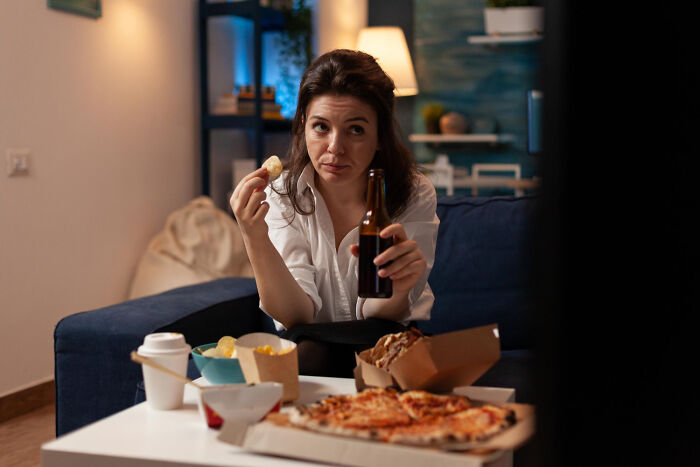 A woman on a couch with fast food and a drink, highlighting potential unhealthy poverty habits when not actively avoided.