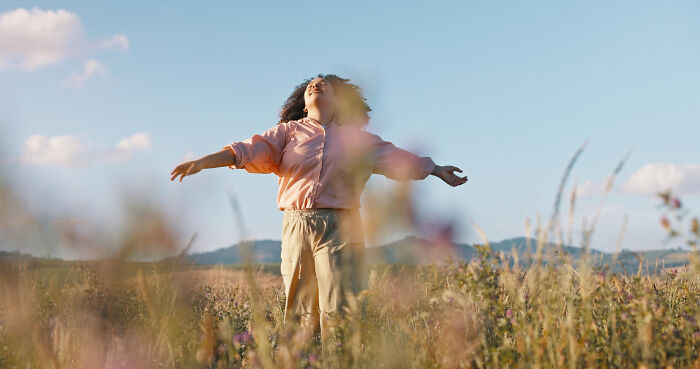 Woman with arms outstretched in a field, symbolizing freedom and the beautiful life.