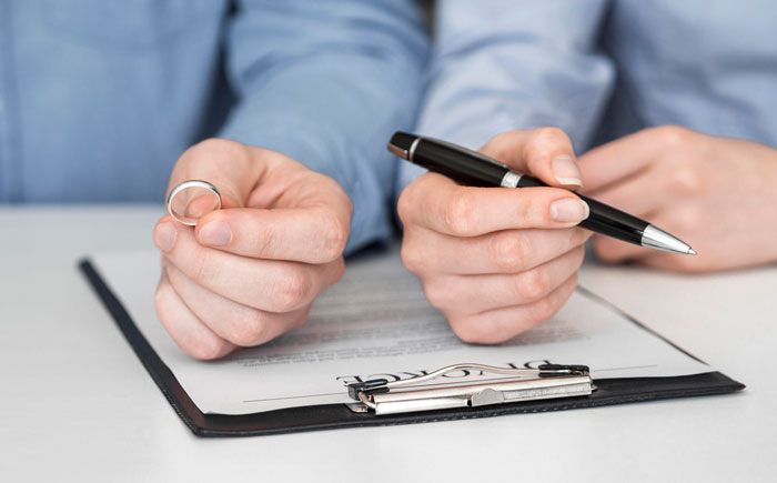 Hands with a wedding ring and a pen over divorce papers, symbolizing a woman leaving her son. Hands with a wedding ring and a pen over divorce papers, symbolizing a woman leaving her son.