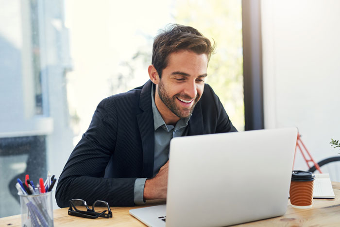 A smiling man on a laptop, representing a colleague's work and how a workplace bully stole credit. A smiling man on a laptop, representing a colleague's work and how a workplace bully stole credit.