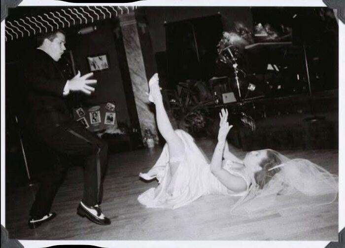 Funny wedding photo of a groom looking shocked as the bride falls on the dance floor, creating an iconic moment.