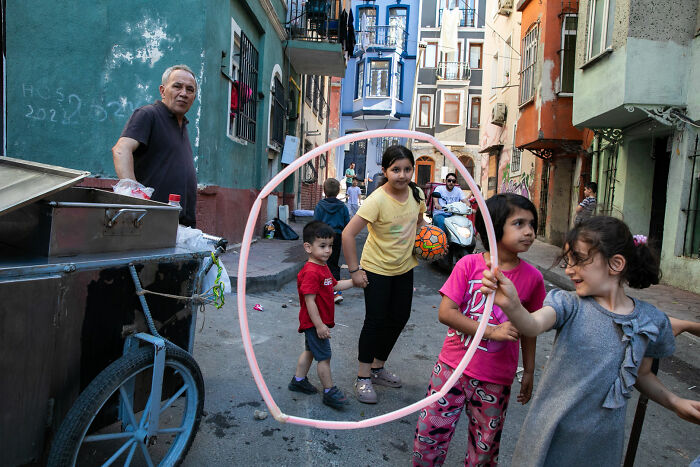 Children play with a large hoop in a narrow street, captured in street photography that turns ordinary scenes into art.