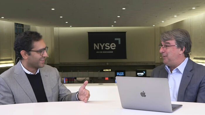 Two men, one resembling the CEO who went viral for firing 900 employees, conversing with a laptop.