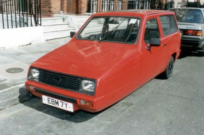 A red Reliant Robin three-wheeled car parked on a street, an example of dry British humor.