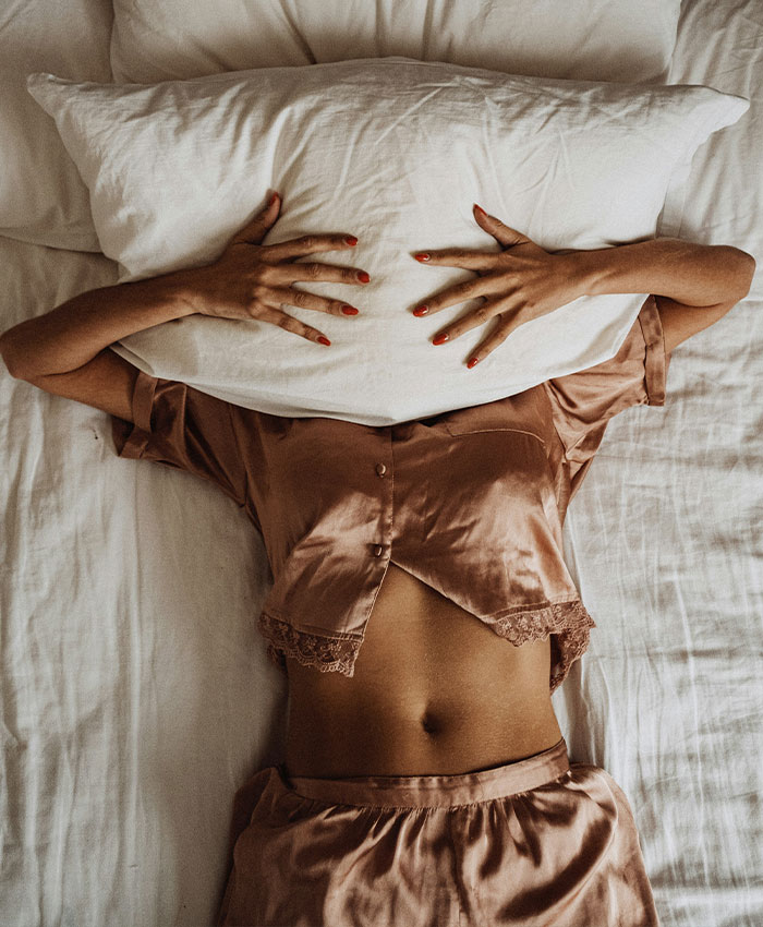 Woman in bed covering her face with a pillow, experiencing hidden perimenopause symptoms.