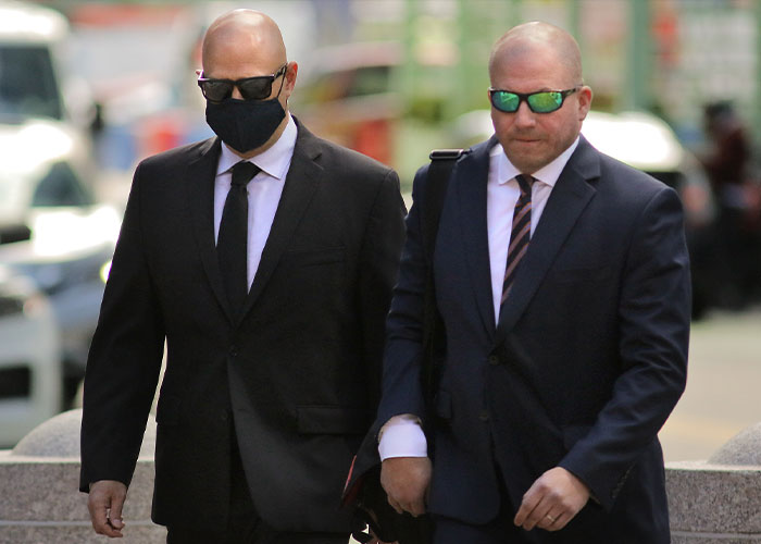Two men in suits and sunglasses, one wearing a mask, walking, connected to the eBay campaign against an old couple's lives.
