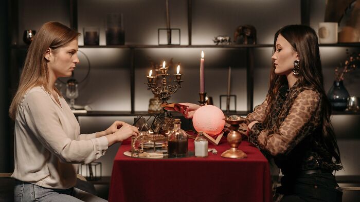 Two women are sitting opposite each other at a table, discussing relationship issues and controlling boyfriend eats.