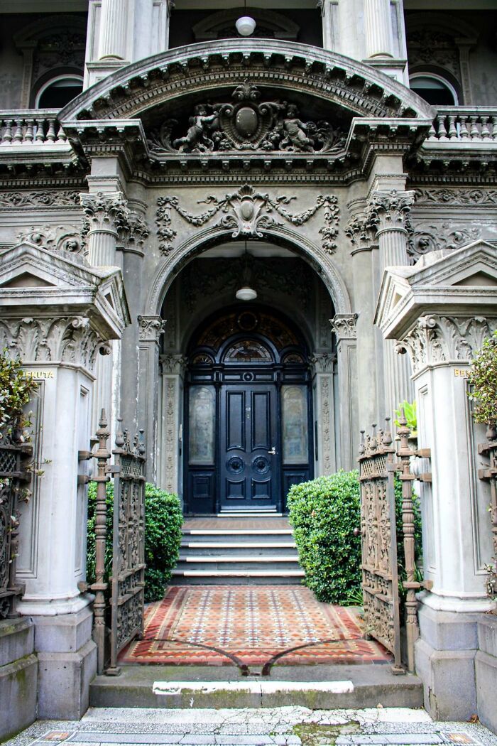 A grand, ornate building entrance with a dark wooden door, decorative stone carvings, and an elegant rug leading to it. This building has so much character.