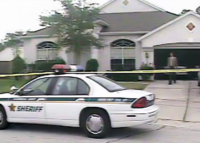 A sheriff's car in front of a house, marked with crime scene tape, related to a serial criminal escape.