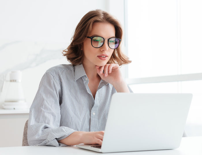 A woman in glasses and a striped shirt typing on a laptop, perhaps reflecting on shameful things that happened at weddings.