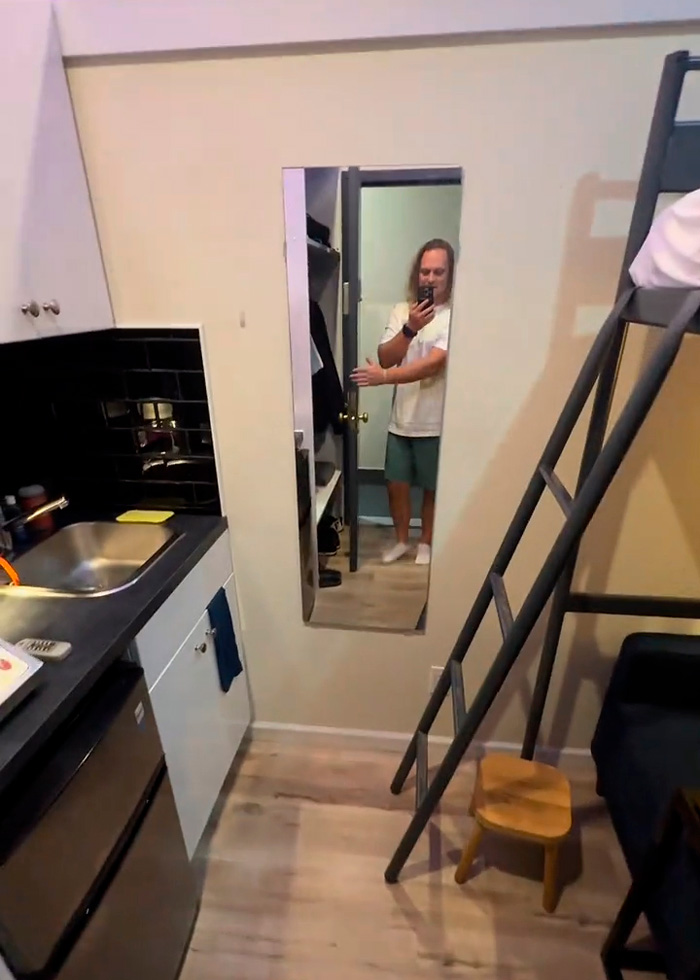 Interior view of a small NYC apartment. The man is reflected in a full-length mirror, showcasing the tight living space. Interior view of a small NYC apartment. The man is reflected in a full-length mirror, showcasing the tight living space.