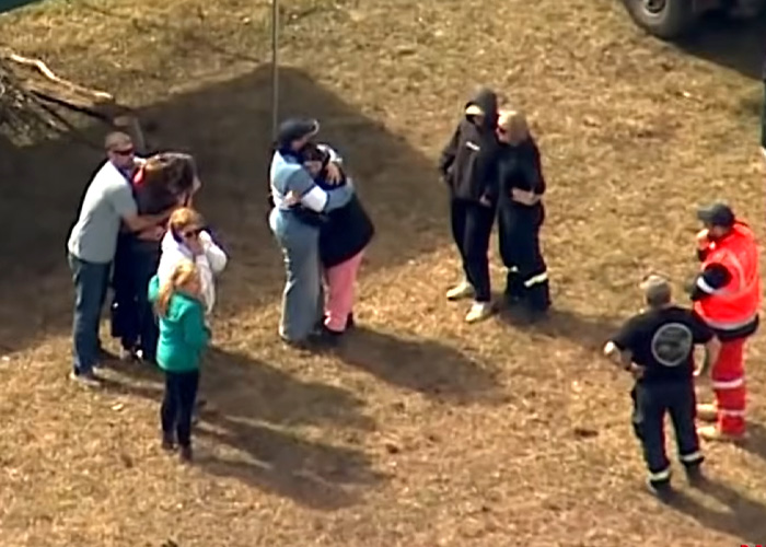 People embracing and consoling each other in a field after the body of the missing teen was found.