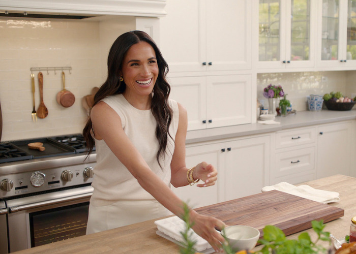 Meghan Markle smiling in a modern kitchen, as former US neighbors expose further revelations about her and Prince Harry.