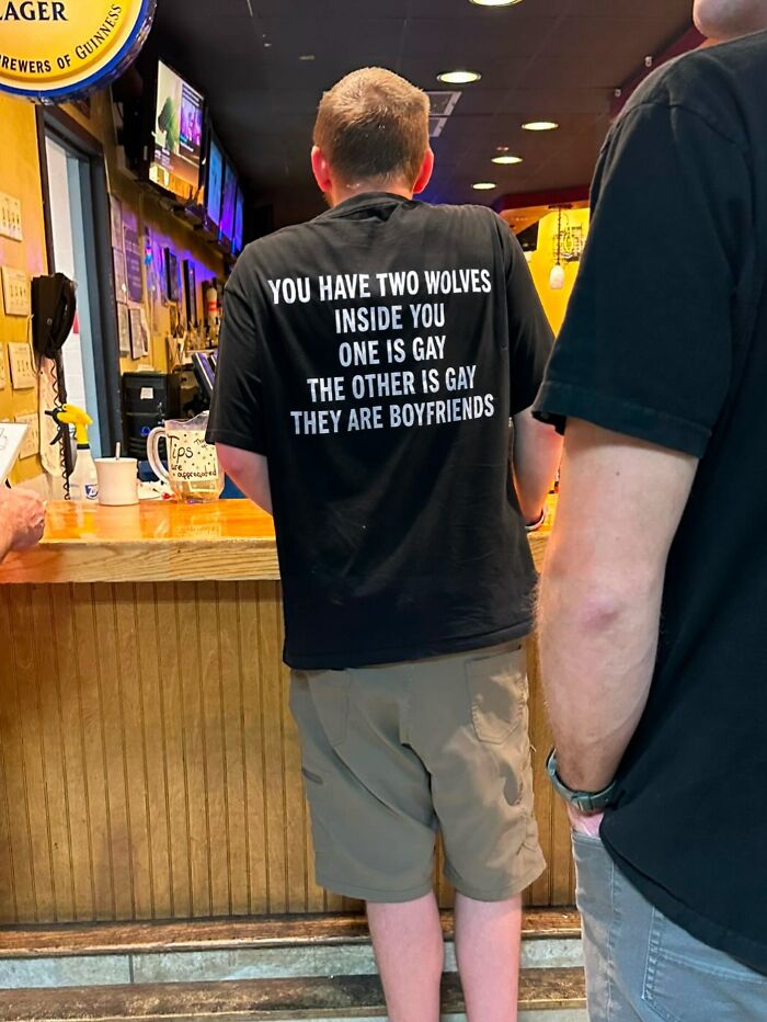 The back of a man's black iconic shirt with the text: YOU HAVE TWO WOLVES INSIDE YOU ONE IS GAY THE OTHER IS GAY THEY ARE BOYFRIENDS.