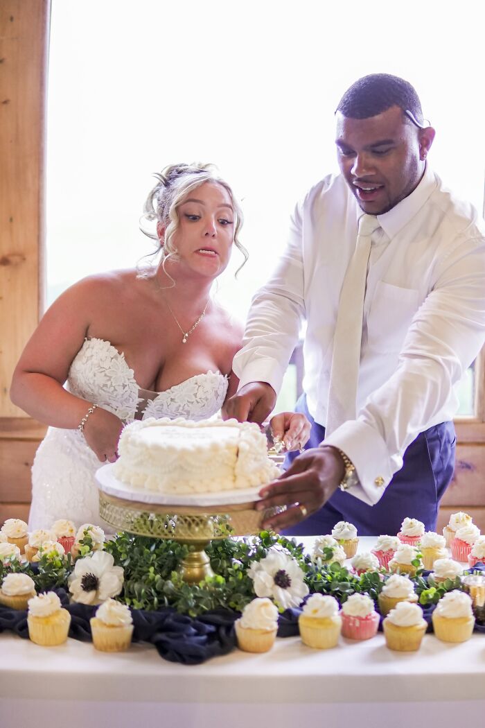 Funny wedding photo of a bride making a silly face while she and the groom cut their wedding cake, an iconic moment.