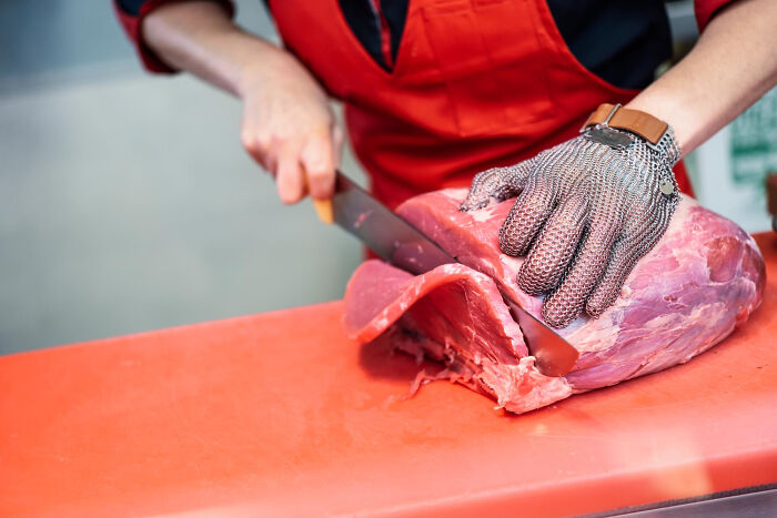 A butcher wearing a chainmail glove cuts a large piece of red meat, revealing a secret.