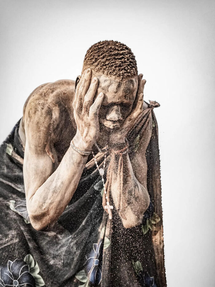 A young boy with a dirt-covered face crouches on the ground, creating shapes from mud. This image won a 2026 European Photography Award.