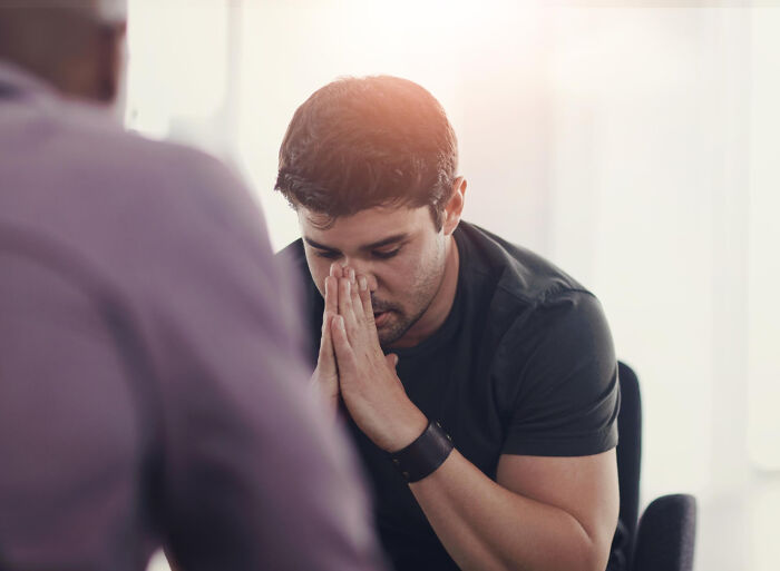 A man with clasped hands looking down, receiving a hard diagnosis from a doctor.