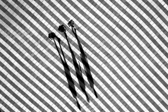 Murat Bakmaz captures the beauty of everyday life: Three people's long shadows stretch across a striped black and white tiled ground.