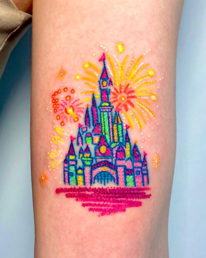 Disney castle tattoo inspired by crayon drawings with colorful fireworks on a person's leg.