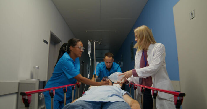 Medical field workers, a nurse and a doctor, attend to a patient on a stretcher in a hospital hallway.