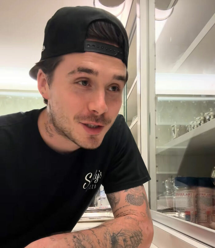 Brooklyn Beckham in a black t-shirt and backward cap, looking focused during his latest cooking video.