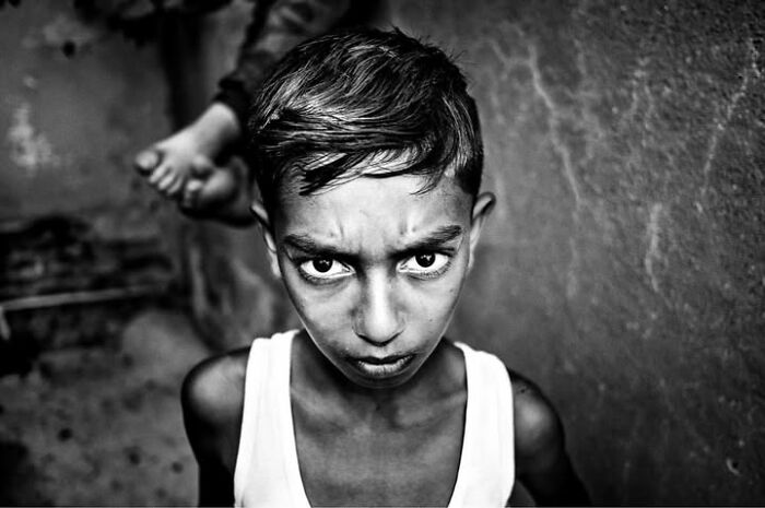 A close-up, black and white street photo of a young boy with furrowed brows, staring intensely at the camera, capturing the intensity of childhood.