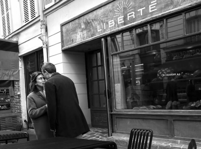 A black and white street photo by Gaspard Claude of a couple in Paris in front of a store with Libérté written on it.
