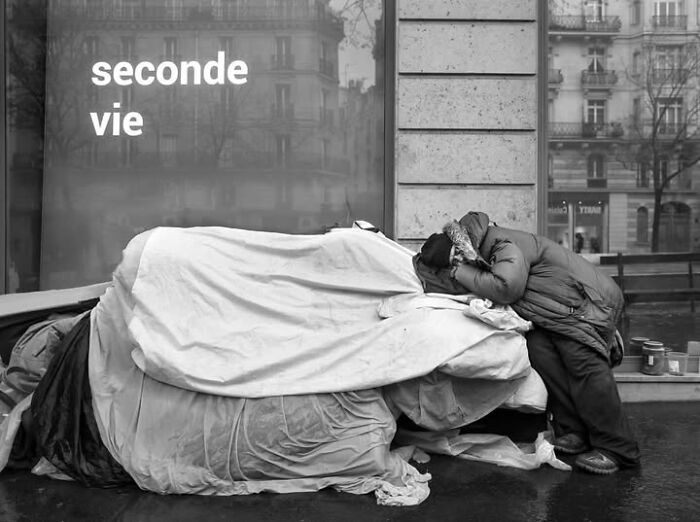 A person sleeping under blankets on a Paris street, showcasing an unseen side of Paris in a perfectly timed photo by Gaspard Claude.