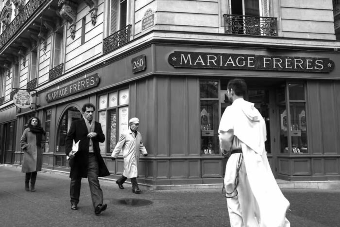 People walking past Mariage Freres in Paris, featuring various individuals and a person in a robe, a perfectly timed street photo.