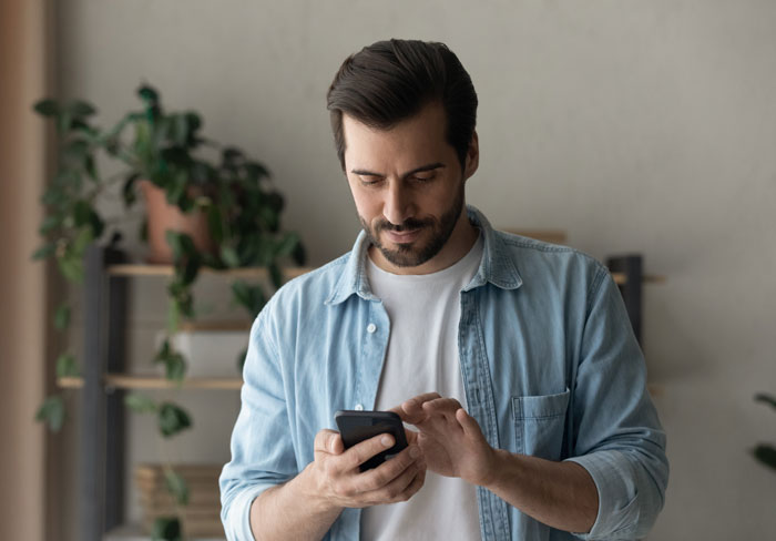 Man in denim shirt scrolling on his phone, showing seriousness about going NC with MIL after she kicked a senior dog. Man in denim shirt scrolling on his phone, showing seriousness about going NC with MIL after she kicked a senior dog.