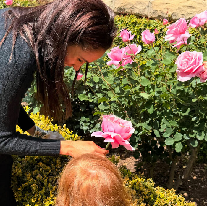 Meghan Markle with a child, smelling a pink rose, relating to her and Prince Harry's return to UK. Meghan Markle with a child, smelling a pink rose, relating to her and Prince Harry's return to UK.