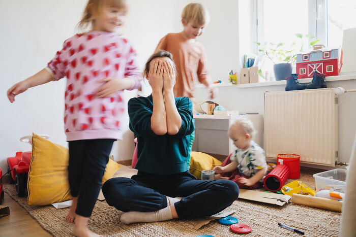 A stressed mother with her face in her hands while her children play around her, depicting dumb reasons couples divorce.