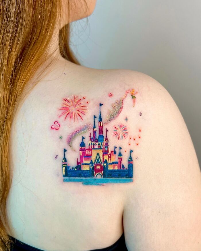 Colorful Disney castle tattoo with Tinkerbell and fireworks on a woman's shoulder, inspired by crayon drawings.