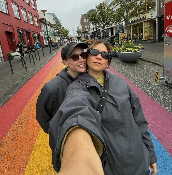 Elliot Page and friend on a rainbow crosswalk, addressing controversy over biology classes and queer/trans people.